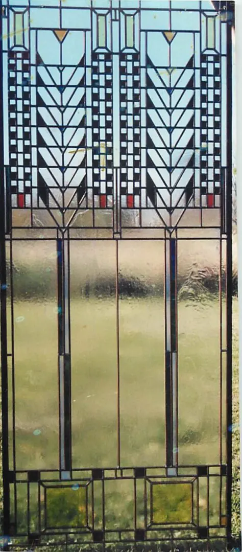 Stained glass panel featuring geometric designs with tall, symmetrical patterns against a blurred outdoor background.