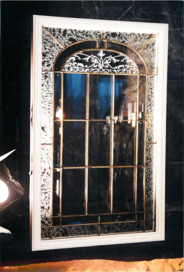 Rectangular mirror with ornate white frame and decorative metal grid, reflecting a dimly lit interior.