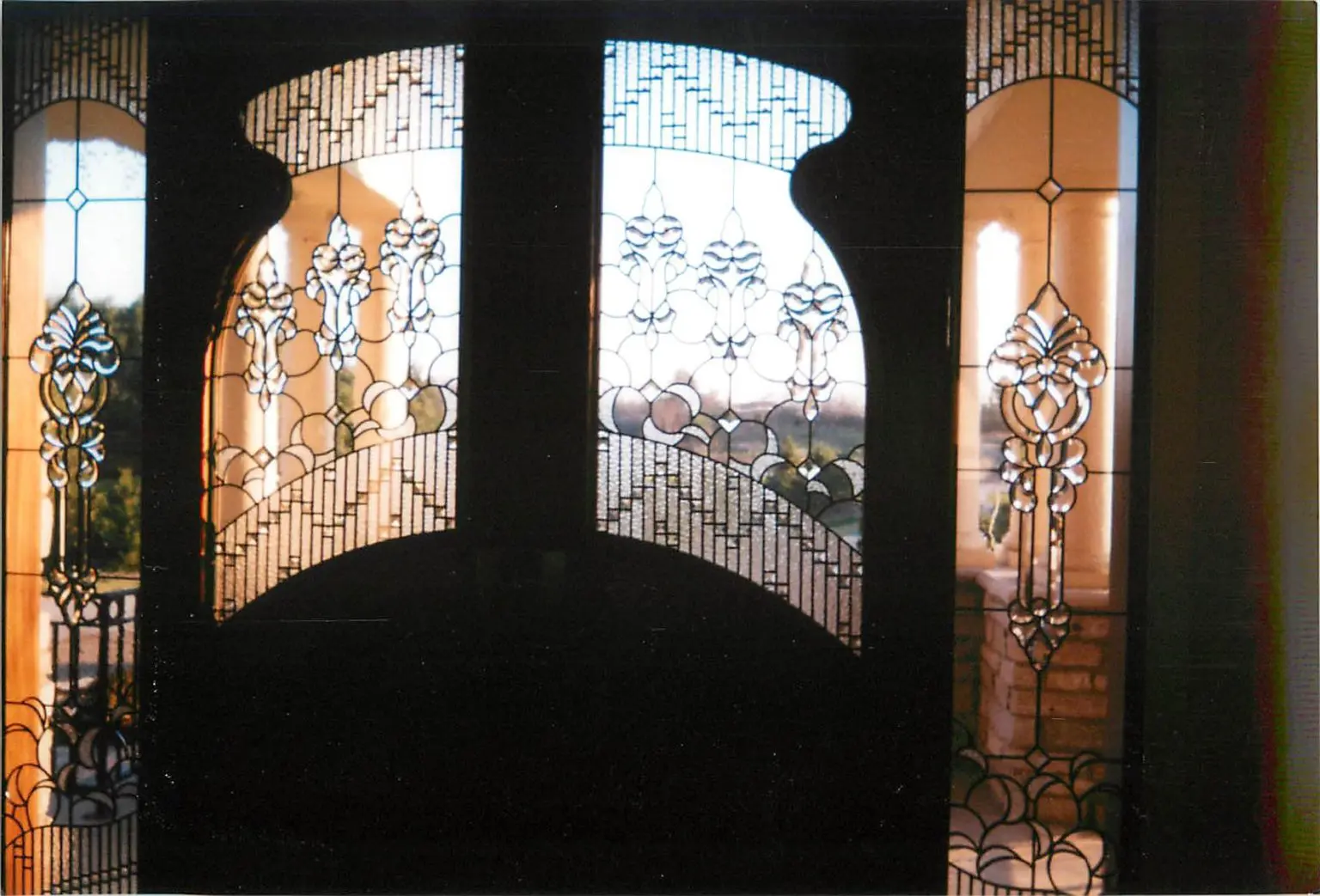 Ornate stained glass doors with floral patterns open to a view of an outdoor balcony and landscape.