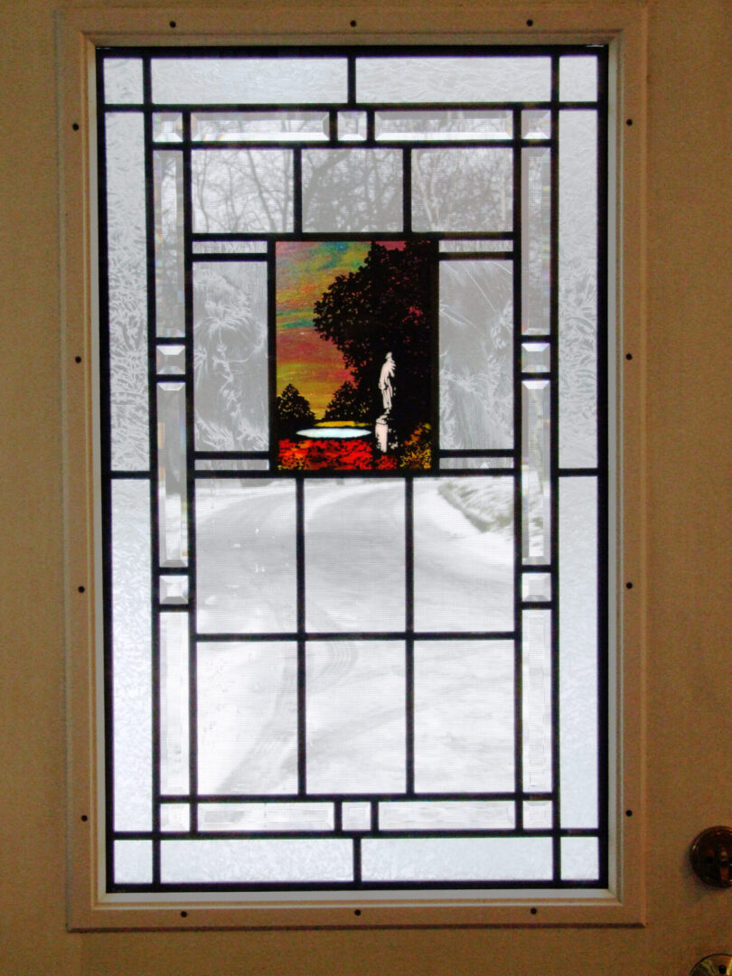 Stained glass door with geometric patterns and a central panel depicting a silhouette of a person against a colorful landscape with trees and sunset.