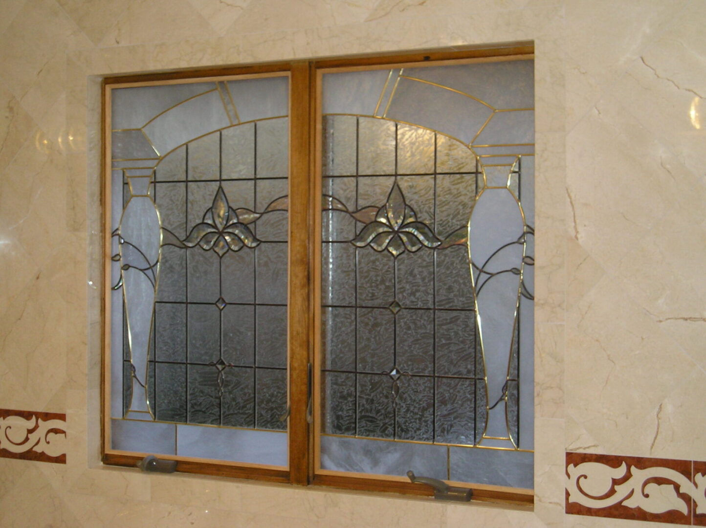 Stained glass window with geometric and floral pattern framed by wooden panels, set in a tiled wall.